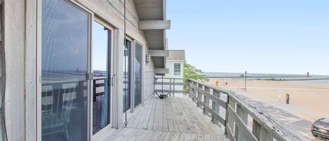 A wooden deck with large sliding glass doors, a metal railing, and a view of the beach.