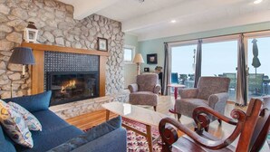 Un salon avec un mur en pierre, une cheminée et un coin salon comprenant des fauteuils à motifs et un canapé bleu.