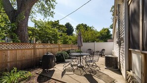 A patio with a round table and chairs, a grill, and a covered umbrella. - Sweet Retreat in South Haven • 2 Blocks from Beach (South Haven)
