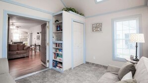 A living room with a high ceiling, a skylight, a sofa, a bookshelf, and a door leading to a kitchen. - Sweet Retreat in South Haven • 2 Blocks from Beach (South Haven)
