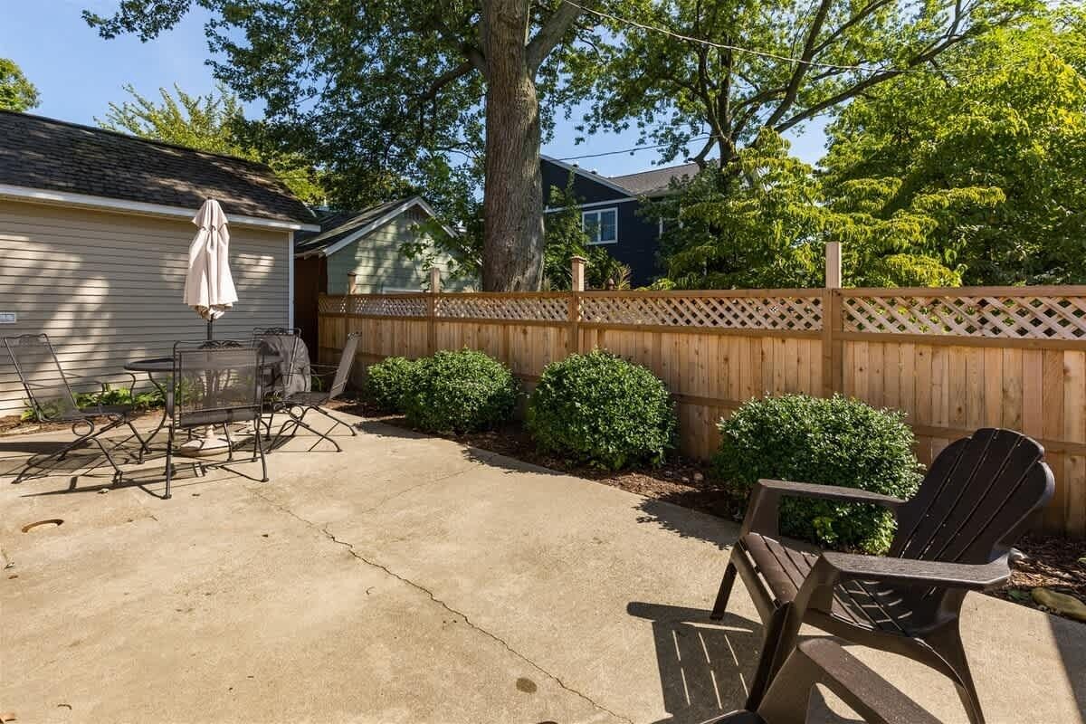 A backyard with a patio table and chairs, a wooden fence, and a large tree.