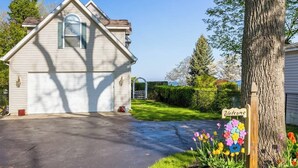 A single-story house with a garage, a welcome sign, and a garden with colorful flowers. - Carriage House (South Haven)