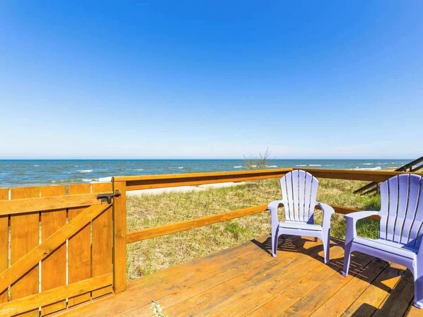 A wooden deck with two Adirondack chairs facing a beach.