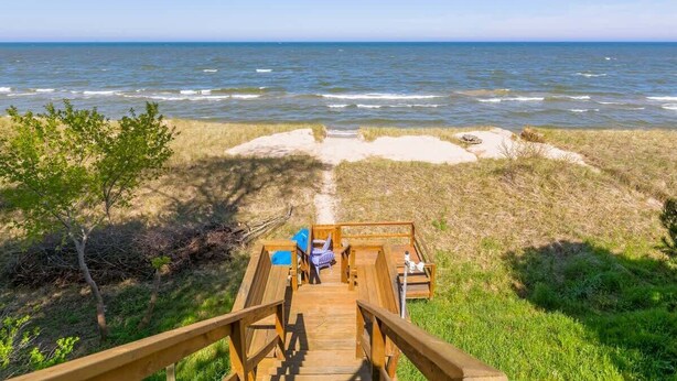 A wooden deck leading to a beach with a clear view of the ocean. - Carriage House (South Haven)