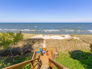 A wooden deck leading to a beach with a clear view of the ocean.