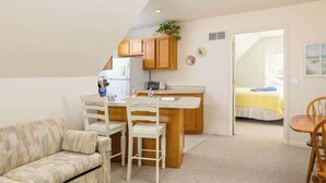 A compact living space with a kitchenette, a sofa, a dining table with chairs, and a bed in the background. - Carriage House (South Haven)
