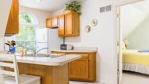 A kitchen with wooden cabinets, a white countertop, and a window with blinds. - Carriage House (South Haven)