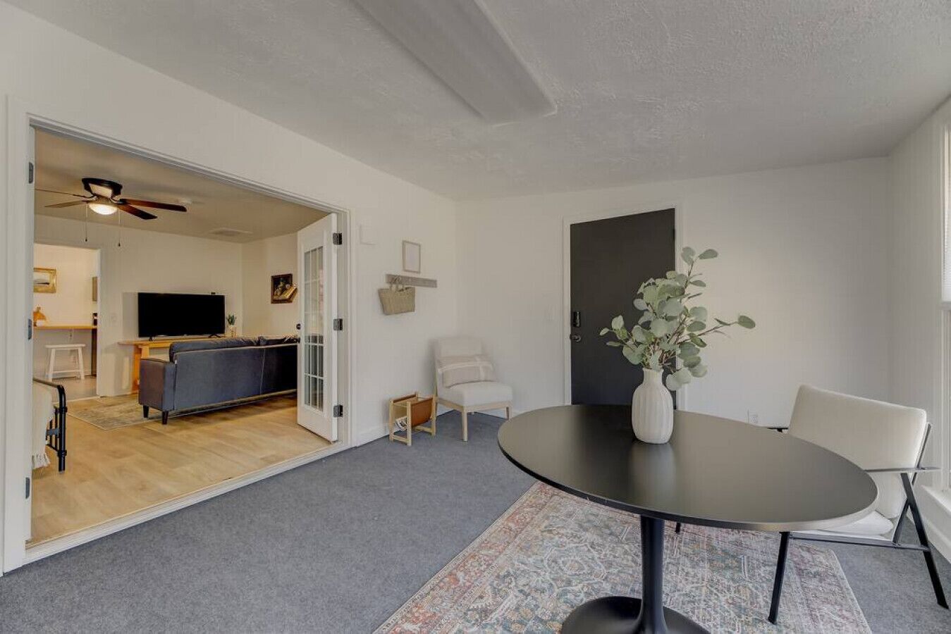 A modern living room with a round table, two chairs, a sofa, and a television in the background.