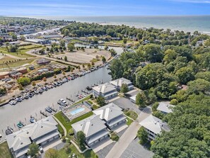 Vista aérea de uma área costeira com um porto de iates, edifícios residenciais e uma praia.