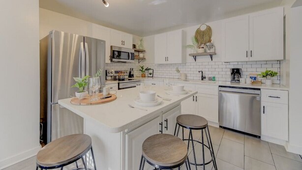 A modern kitchen with white cabinets, stainless steel appliances, and a central island with stools. - Modern 4 BR Apt - Mins to USC, ZOO & Ft Jackson (Columbia)