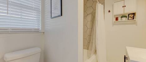 Une salle de bain comprenant des toilettes, une douche avec un mur recouvert de carreaux hexagonaux et un meuble blanc avec une étagère.