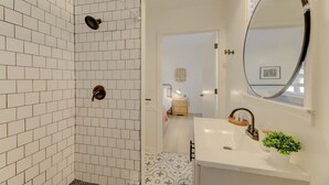 A bathroom with white subway tiles, a shower with a dark faucet, a white sink with a gold faucet, and a round mirror. - Modern 4 BR Apt - Mins to USC, ZOO & Ft Jackson (Columbia)