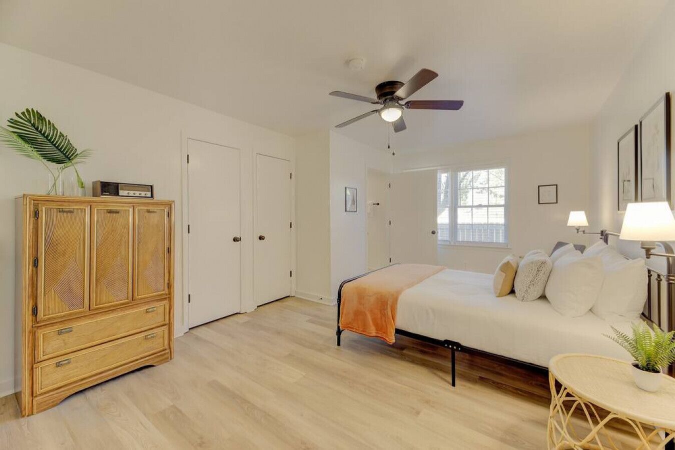 A bedroom with a bed, a ceiling fan, a wardrobe, and a small table with a plant.