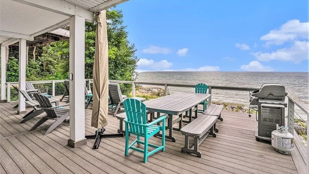 Eine überdachte Terrasse mit Gartenmöbeln, einem Grill und Blick auf den Ozean.