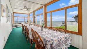 Ein Essbereich mit Meerblick, Holzstühle, ein Tisch mit gemustertem Tischläufer und ein Deckenventilator.