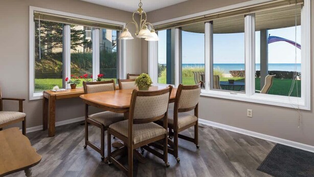 Un área de comedor con una mesa y sillas de madera, ventanas amplias con vistas a un campo de golf y una lámpara colgante.