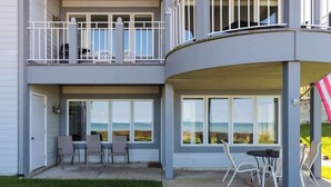 Una casa de dos pisos con un patio cubierto, mobiliario exterior y grandes ventanales con vistas panorámicas.