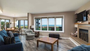 Amplia sala de estar con un ventanal que ofrece vistas al mar, una chimenea y un televisor montado en la pared.