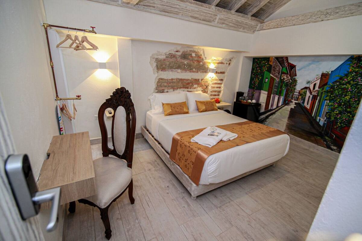 Una camera da letto con un letto, una sedia, una scrivania, una lampada a parete e un affresco.