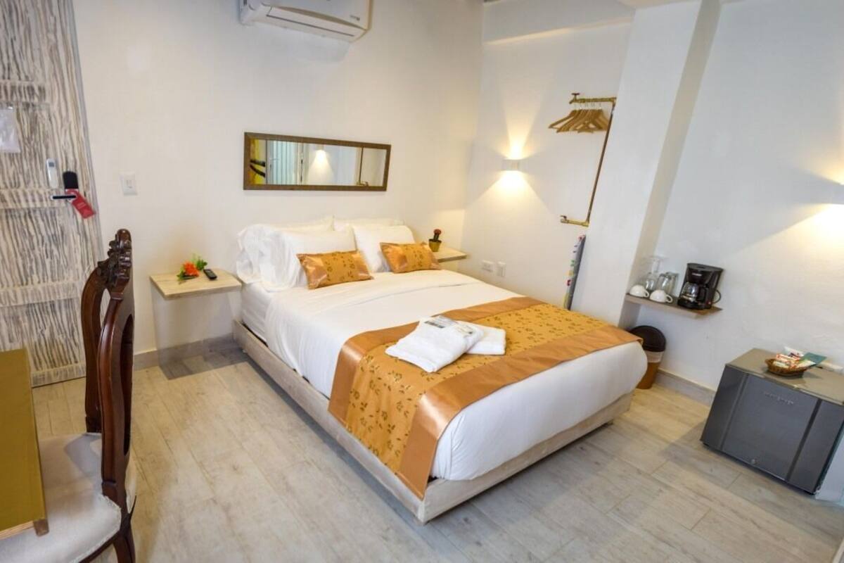 Una camera d'albergo con un letto, comodini, una sedia, una scrivania, un armadio e un piccolo mobiletto.