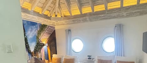 A room with two beds, a wooden ceiling, and a mural on the wall.