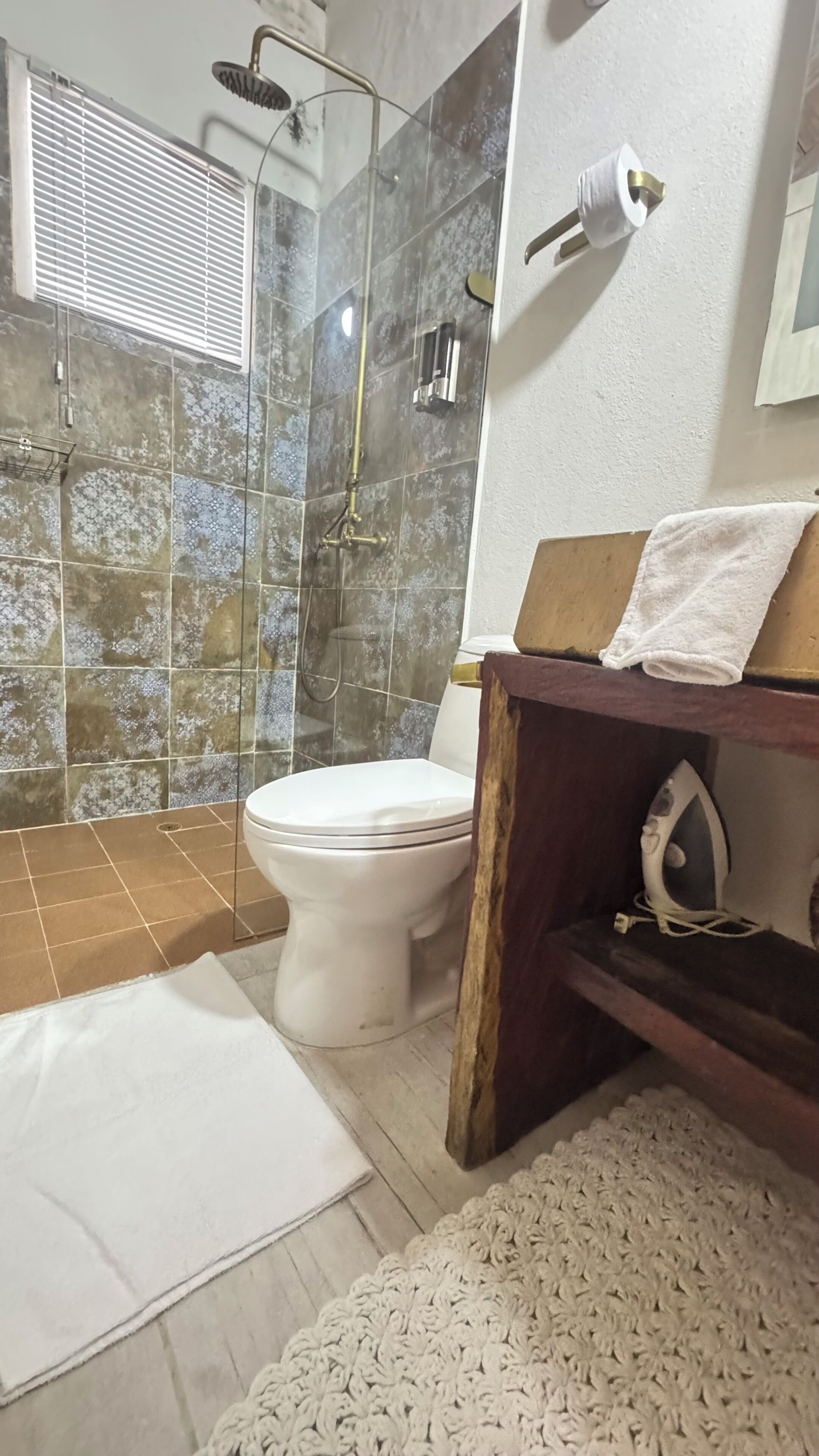 A bathroom with a shower, toilet, and a wooden vanity with a towel.