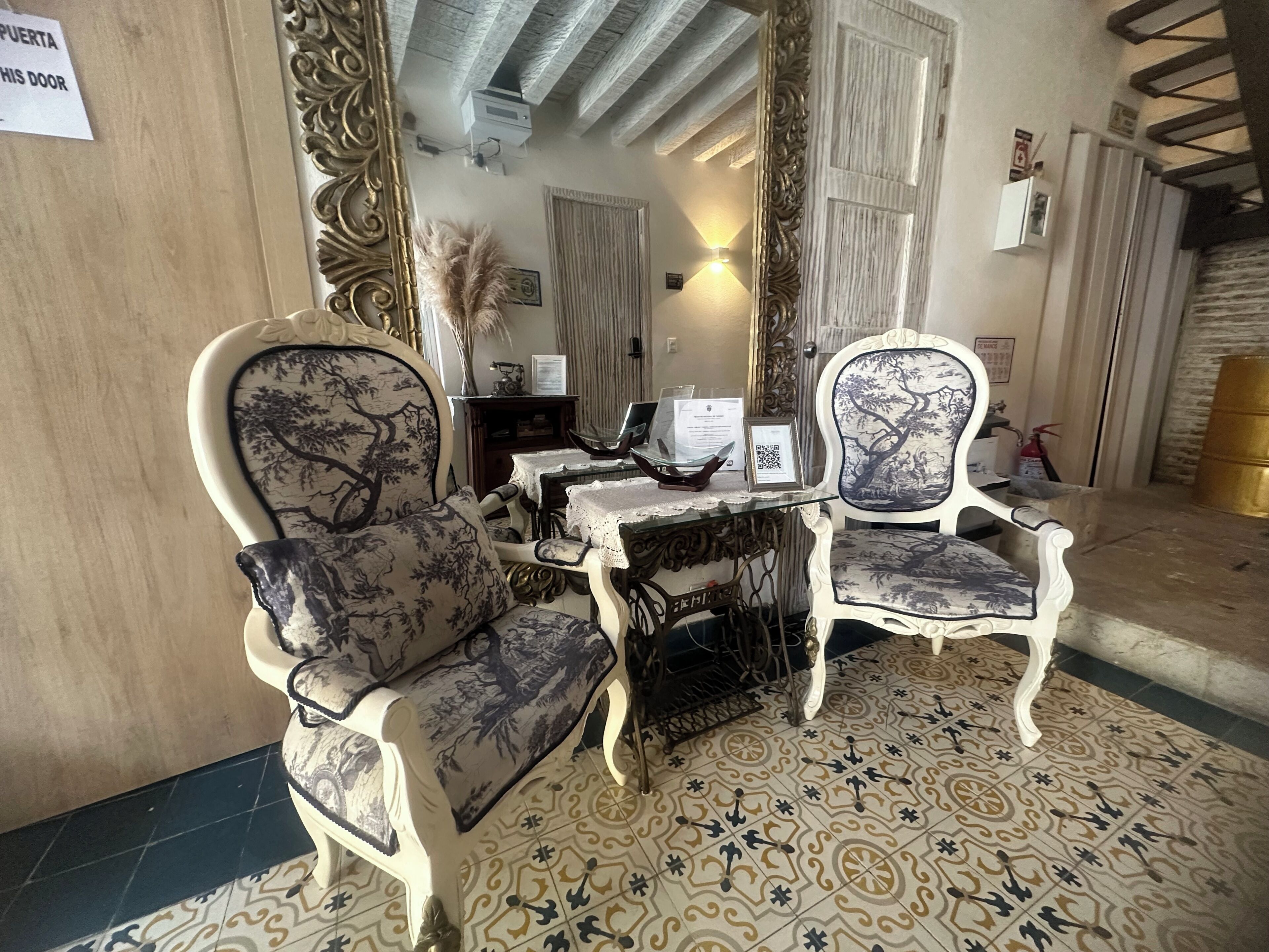A room with ornate furniture, a patterned floor, and a mirror reflecting the room's interior.