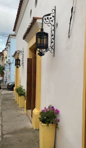 A narrow street with buildings featuring yellow and white facades, black wrought iron lanterns, and potted plants. - Hotel boutique callecitas de san diego (Cartagena)
