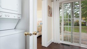 A room with a white appliance, a door with brass handles, and a view of a backyard through a glass door. - Beach Grass, 2 BR, South Haven, Walk to the Beach (South Haven)