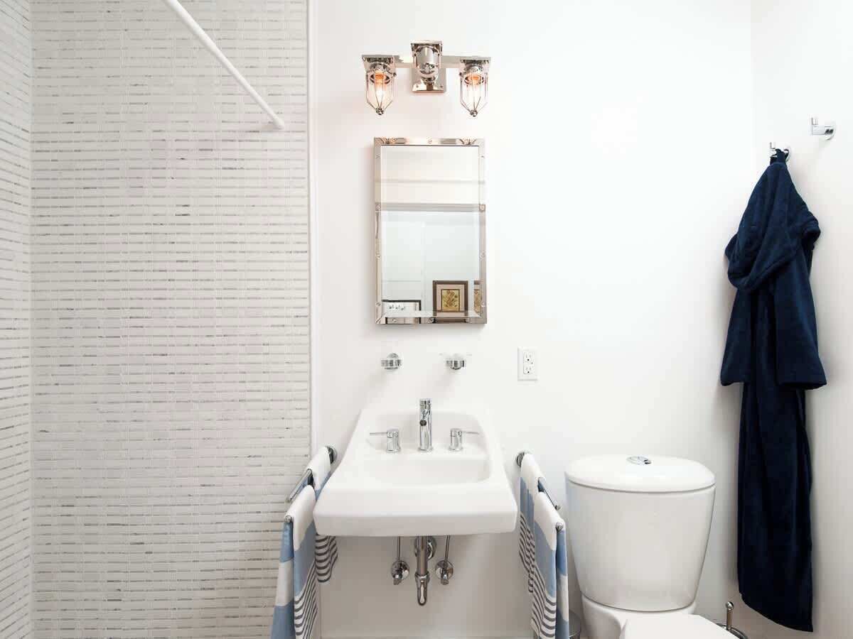 A bathroom with a white sink, a mirror, and a toilet. There is a towel hanging on the wall.