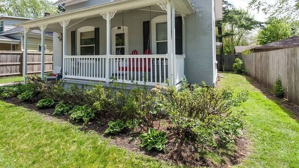 Ein zweistöckiges Haus mit Veranda, einem eingezäunten Garten und einem gepflegten Rasen.