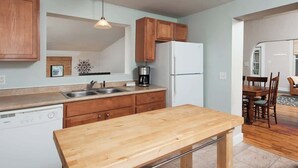 Eine kompakte Küche mit Holzausstattung, einem weißen Kühlschrank, einer Kaffeemaschine und einem Geschirrspüler.