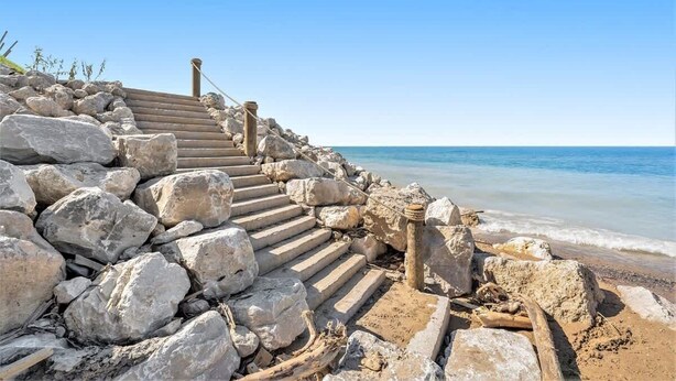 A stone staircase leading to a beach with a clear view of the ocean.