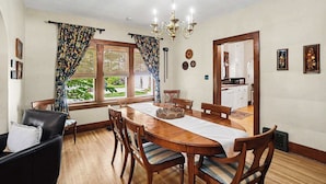 Une salle à manger avec une table en bois, des chaises, un lustre et une vue sur l’extérieur.