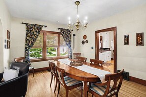 A dining room with a wooden table, chairs, a chandelier, and a view of the outdoors.