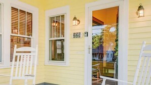 Une maison jaune avec un revêtement blanc, le numéro « 225 » sur la porte et deux fauteuils à bascule sur le porche.
