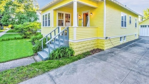 Une maison jaune de plain-pied, dotée d’un porche à l’avant, d’un escalier et d’un garage.