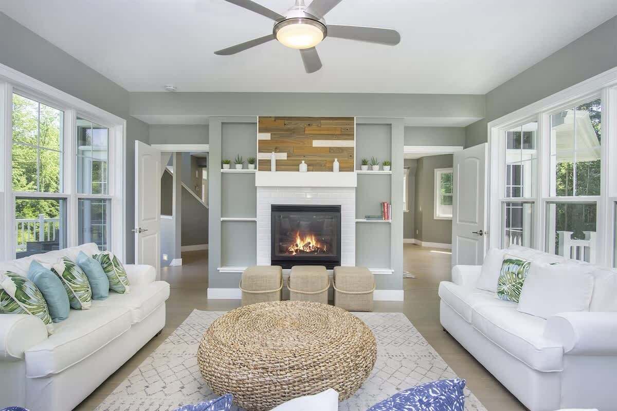 Una sala de estar con chimenea, sofás blancos y un ventilador de techo.