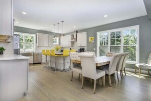 Una cocina moderna con armarios blancos, una isla central y un comedor con mesa y sillas blancas.
