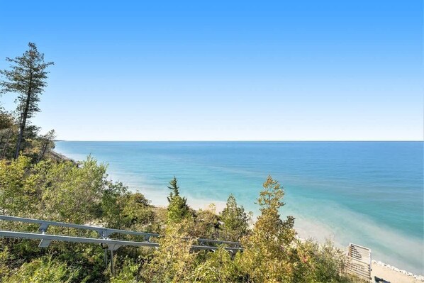 Vista costera con cielo despejado, una playa y un área boscosa con una estructura de madera.