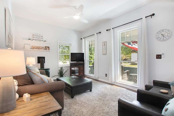 A living room with a sofa, a coffee table, a TV, and a large window with a view of the outdoors.