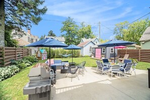 A backyard patio with outdoor furniture, a grill, and umbrellas.