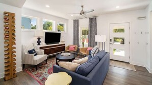 A living room with a sofa, armchairs, a TV, and a ceiling fan. - SH Cottage (South Haven)