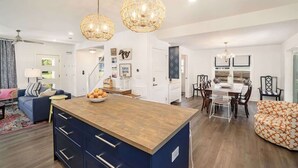 A modern kitchen with a central island, pendant lighting, and a dining area with a table and chairs. - SH Cottage (South Haven)