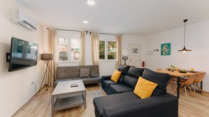 Ett modernt vardagsrum med en platt-TV, soffa, soffbord och en matplats med stolar och ett bord.