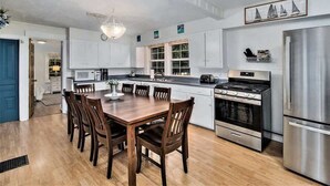 Una cocina moderna con armarios blancos, un refrigerador de acero inoxidable y un comedor con sillas y una mesa de madera.
