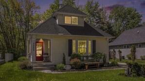 Une maison à deux étages avec un porche à l’avant, un petit jardin et une porte de garage bien visible.