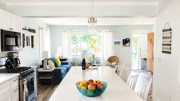 A modern kitchen with white cabinetry, a central island with fruit, and a dining area with white chairs. - Mail Legacy Cottage in South Haven • Dogs Welcome (South Haven)