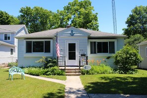 A two-story house with a front porch, a mailbox, and a small garden with a bench.