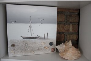 Una pintura de un velero sobre una orilla arenosa, con gaviotas, un muro de piedra y una concha marina.